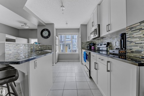 Kitchen featuring a breakfast bar area, stainless steel appliances, tasteful backsplash, white cabinets, and a textured ceiling - #127 2905 141 Street, Edmonton, AB - Indoor Photo Showing Kitchen With Upgraded Kitchen