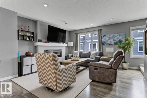 Living area with wood finished floors, a glass covered fireplace, a textured ceiling, and recessed lighting - #127 2905 141 Street, Edmonton, AB - Indoor Photo Showing Living Room With Fireplace