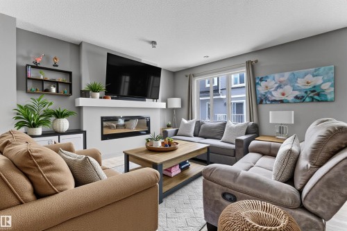 Living area featuring a glass covered fireplace, light wood-style flooring, and a textured ceiling - #127 2905 141 Street, Edmonton, AB - Indoor Photo Showing Living Room With Fireplace