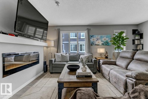 Living room with a glass covered fireplace, a textured ceiling, and light wood-type flooring - #127 2905 141 Street, Edmonton, AB - Indoor Photo Showing Living Room With Fireplace