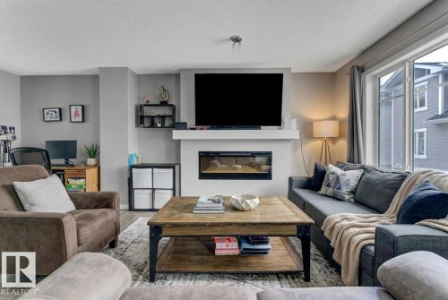 Living room featuring wood finished floors, a glass covered fireplace, and a textured ceiling - #127 2905 141 Street, Edmonton, AB - Indoor Photo Showing Living Room With Fireplace