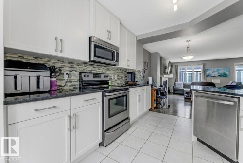 Kitchen with stainless steel appliances, dark stone countertops, white cabinetry, open floor plan, and decorative light fixtures - #127 2905 141 Street, Edmonton, AB - Indoor Photo Showing Kitchen With Upgraded Kitchen