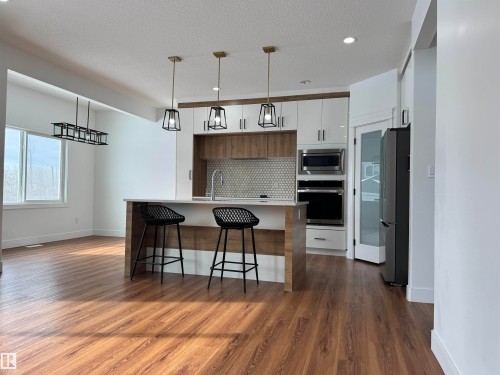 Kitchen with modern cabinets, stainless steel appliances, a kitchen breakfast bar, a kitchen island with sink, and dark wood-style flooring - 1703 152 Avenue, Edmonton, AB - Indoor Photo Showing Kitchen