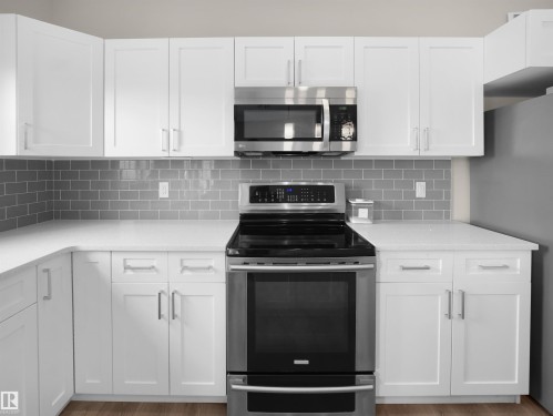 Kitchen featuring stainless steel appliances, white cabinets, light wood-style flooring, tasteful backsplash, and light stone counters - 8921 217 St Nw, Edmonton, AB - Indoor Photo Showing Kitchen With Upgraded Kitchen