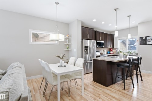 Kitchen featuring dark wood finish cabinets, stainless steel appliances, a kitchen island with sink, a breakfast bar area, and light wood-type flooring - 149 Hawks Ridge Boulevard, Edmonton, AB - Indoor