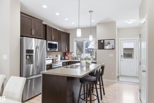 Kitchen with dark wood finish cabinets, stainless steel appliances, a kitchen island with sink, a kitchen breakfast bar, and light countertops - 149 Hawks Ridge Boulevard, Edmonton, AB - Indoor Photo Showing Kitchen With Double Sink With Upgraded Kitchen