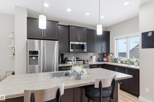 Kitchen featuring a breakfast bar, stainless steel appliances, dark wood finish cabinetry, light wood-type flooring, and tasteful backsplash - 149 Hawks Ridge Boulevard, Edmonton, AB - Indoor