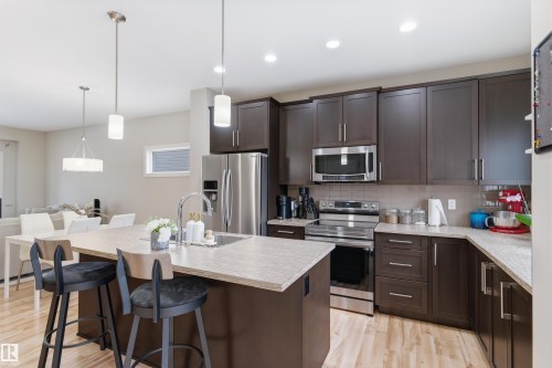 Kitchen with stainless steel appliances, dark wood finish cabinets, a kitchen bar, light wood-style flooring, and a center island with sink - 149 Hawks Ridge Boulevard, Edmonton, AB - Indoor Photo Showing Kitchen With Upgraded Kitchen