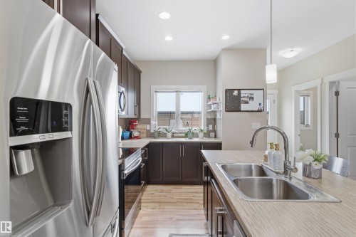 Kitchen featuring stainless steel appliances, dark wood finish cabinets, light countertops, and pendant lighting - 149 Hawks Ridge Boulevard, Edmonton, AB - Indoor Photo Showing Kitchen With Double Sink With Upgraded Kitchen