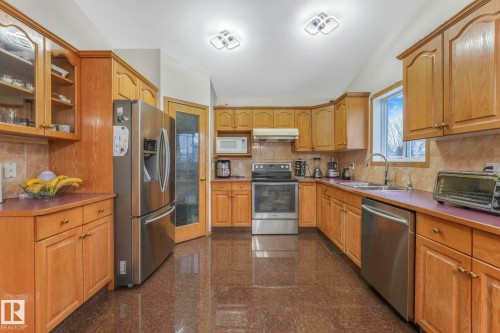 Kitchen with granite tiled floors, appliances with stainless steel finishes, glass insert cabinets, tasteful backsplash, and under cabinet range hood - 4720 150 Avenue, Edmonton, AB - Indoor Photo Showing Kitchen With Double Sink
