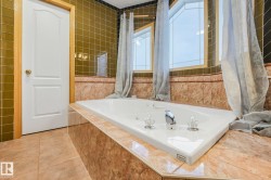 Bathroom featuring light tile patterned flooring, a tub with jets, and tile walls - 