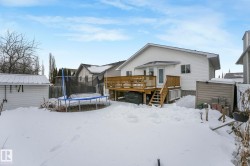 Snow covered rear of property with a trampoline, a wooden deck, stairs, and a storage shed - 