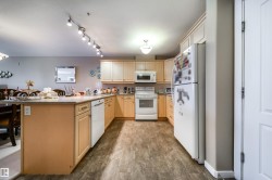 Kitchen featuring a peninsula, white appliances, light wood finish cabinetry, decorative backsplash, and a kitchen breakfast bar - 