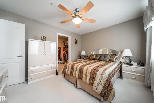 Bedroom with a walk in closet, a ceiling fan, and light colored carpet - 237 278 Suder Greens Drive, Edmonton, AB - Indoor Photo Showing Bedroom