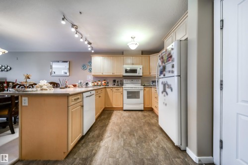 Kitchen featuring a peninsula, white appliances, light wood finish cabinetry, decorative backsplash, and a kitchen breakfast bar - 237 278 Suder Greens Drive, Edmonton, AB - Indoor Photo Showing Kitchen