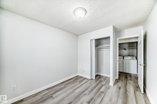 Unfurnished bedroom featuring a textured ceiling, washing machine and clothes dryer, light wood-type flooring, and a closet - 23 1503 Mill Woods Road E, Edmonton, AB - Indoor Photo Showing Other Room