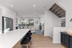 Kitchen with freestanding refrigerator, a kitchen bar, recessed lighting, open floor plan, and light wood-style flooring. Living area with stairway, light wood-style flooring, and recessed lighting, and corner wrapped windows. - 