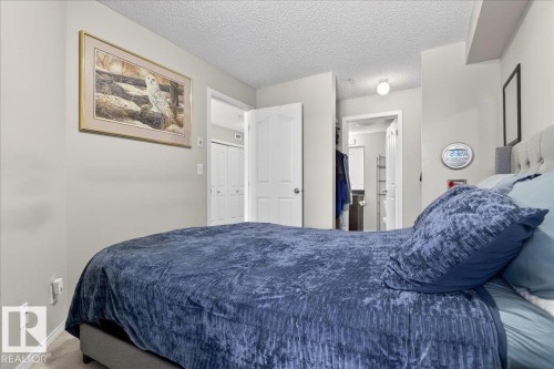 Carpeted bedroom featuring a textured ceiling and ensuite bathroom - 305 12045 22 Avenue, Edmonton, AB - Indoor Photo Showing Bedroom