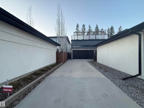 Contemporary architecture featuring a sleek black garage door, a concrete driveway, and an upper-level patio with opaque panel railings - 10038 142 Street, Edmonton, AB - Outdoor