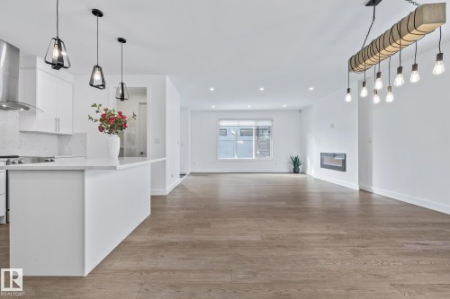 Kitchen featuring white cabinets, decorative light fixtures, light wood finished floors, and a center island - 10038 142 Street, Edmonton, AB - Indoor