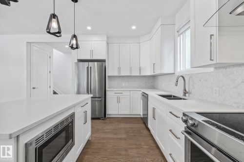 Kitchen with stainless steel appliances, dark wood-type flooring, white cabinets, and range hood - 10038 142 Street, Edmonton, AB - Indoor Photo Showing Kitchen With Double Sink With Upgraded Kitchen