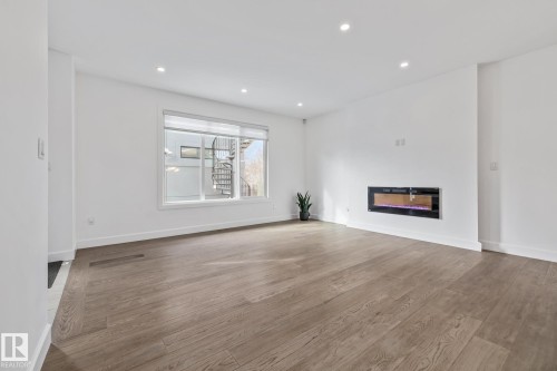 Unfurnished living room featuring wood-type flooring, recessed lighting, and a glass covered fireplace - 10038 142 Street, Edmonton, AB - Indoor Photo Showing Other Room With Fireplace