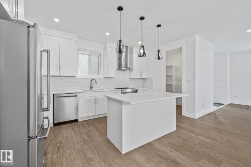 Kitchen with stainless steel appliances, a center island, light wood finished floors, and tasteful backsplash - 10038 142 Street, Edmonton, AB - Indoor Photo Showing Kitchen With Upgraded Kitchen
