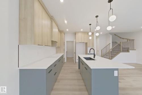 Kitchen featuring light wood finished floors, modern cabinets, pendant lighting, a center island with sink, and light stone counters - 3158 Magpie Way, Edmonton, AB - Indoor Photo Showing Kitchen With Double Sink With Upgraded Kitchen