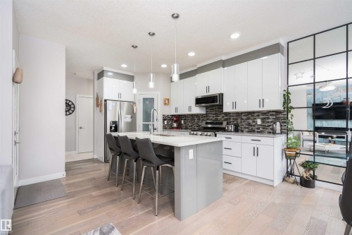 Kitchen featuring a breakfast bar, pendant lighting, a center island with sink, stainless steel appliances, and light wood-style flooring - 43 1703 16 Avenue, Edmonton, AB - Indoor Photo Showing Kitchen With Upgraded Kitchen