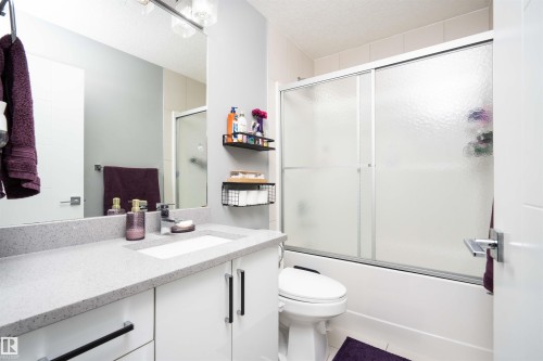 Full bathroom featuring vanity, combined bath / shower with glass door, a textured ceiling, and light tile patterned floors - 43 1703 16 Avenue, Edmonton, AB - Indoor Photo Showing Bathroom