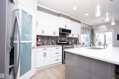 Two tone kitchen featuring stainless steel appliances, dual tone cabinets, tasteful backsplash, light stone countertops, and light wood-style flooring - 43 1703 16 Avenue, Edmonton, AB - Indoor Photo Showing Kitchen With Double Sink With Upgraded Kitchen