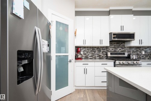 Dual tone kitchen featuring stainless steel appliances, light stone countertops, light wood-style floors, backsplash, and modern cabinets - 43 1703 16 Avenue, Edmonton, AB - Indoor Photo Showing Kitchen