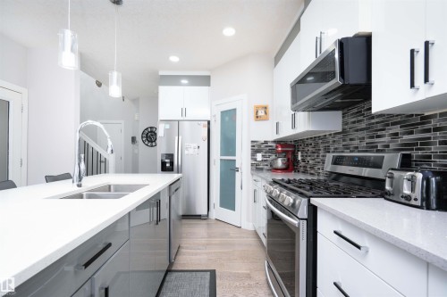 Dual tone kitchen with stainless steel appliances, dual tone cabinetry, light wood-style flooring, light stone counters, and pendant lighting - 43 1703 16 Avenue, Edmonton, AB - Indoor Photo Showing Kitchen With Double Sink With Upgraded Kitchen