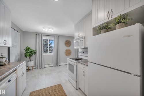 Kitchen featuring white appliances, white cabinets, a baseboard radiator, and light countertops - 201 237 Woodvale Road W, Edmonton, AB - Indoor Photo Showing Kitchen