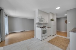 Kitchen featuring white appliances, a baseboard heating unit, and white cabinets - 