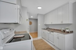 Kitchen with white appliances, white cabinetry, and dark countertops - 