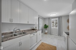 Kitchen with white appliances, white cabinets, dark countertops, and baseboard heating - 