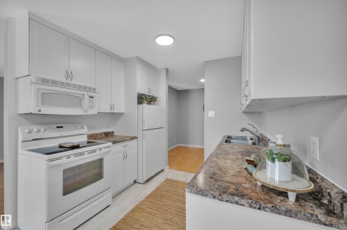 Kitchen featuring white appliances and white cabinetry - 201 237 Woodvale Road W, Edmonton, AB - Indoor Photo Showing Kitchen With Double Sink