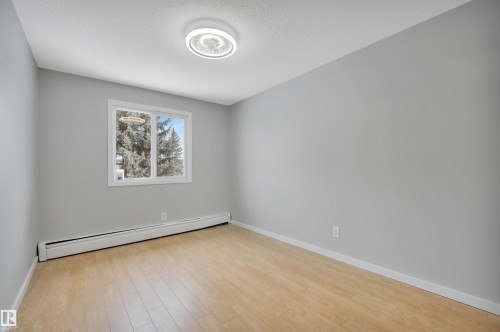 Unfurnished room featuring a baseboard heating unit, light wood finished floors, and a textured ceiling - 201 237 Woodvale Road W, Edmonton, AB - Indoor Photo Showing Other Room