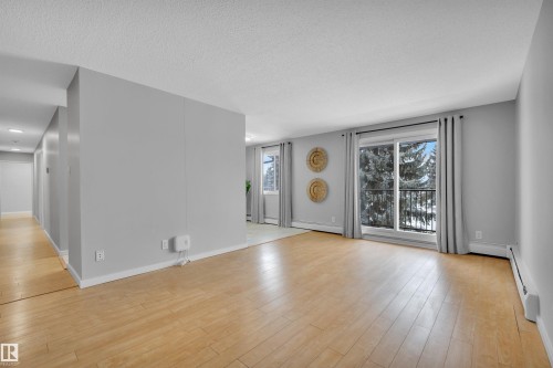 Unfurnished living room with baseboard heating, light wood-style floors, and a textured ceiling - 201 237 Woodvale Road W, Edmonton, AB - Indoor