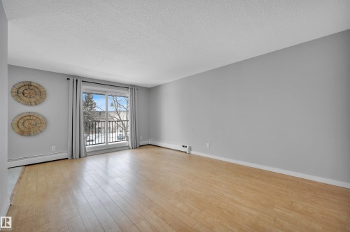 Empty room featuring a baseboard radiator, a textured ceiling, and light wood-style floors - 201 237 Woodvale Road W, Edmonton, AB - Indoor Photo Showing Other Room