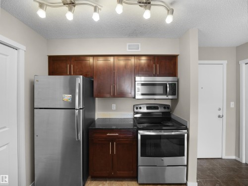 Kitchen featuring stainless steel appliances, a textured ceiling, and dark stone counters - 422 5816 Mullen Place, Edmonton, AB - Indoor Photo Showing Kitchen