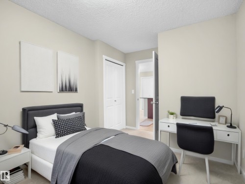 Bedroom with light colored carpet, a textured ceiling, a desk, and a closet - 422 5816 Mullen Place, Edmonton, AB - Indoor Photo Showing Bedroom