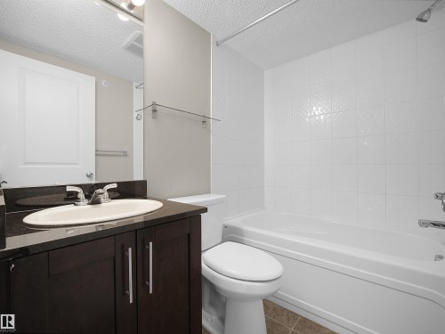 Bathroom featuring vanity, a textured ceiling, bathing tub / shower combination, and dark tile patterned floors - 422 5816 Mullen Place, Edmonton, AB - Indoor Photo Showing Bathroom