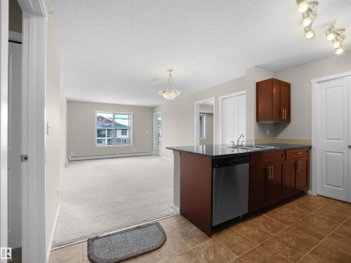 Kitchen with dark colored carpet, a peninsula, dishwasher, a textured ceiling, and open floor plan - 422 5816 Mullen Place, Edmonton, AB - Indoor Photo Showing Kitchen With Double Sink