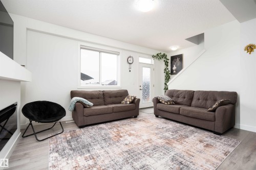 Living room featuring light wood-style floors and a glass covered fireplace - 24 2072 Wonnacott Way, Edmonton, AB - Indoor Photo Showing Living Room