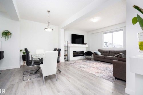 Dining room with a glass covered fireplace and light wood finished floors - 24 2072 Wonnacott Way, Edmonton, AB - Indoor Photo Showing Living Room With Fireplace