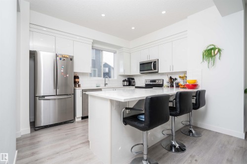 Kitchen featuring stainless steel appliances, a breakfast bar, a peninsula, white cabinets, and recessed lighting - 24 2072 Wonnacott Way, Edmonton, AB - Indoor Photo Showing Kitchen With Stainless Steel Kitchen With Upgraded Kitchen