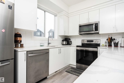 Kitchen with stainless steel appliances, light stone countertops, white cabinets, light wood-style flooring, and backsplash - 24 2072 Wonnacott Way, Edmonton, AB - Indoor Photo Showing Kitchen