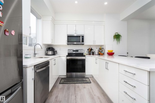 Kitchen featuring stainless steel appliances, white cabinetry, light wood finished floors, light stone countertops, and recessed lighting - 24 2072 Wonnacott Way, Edmonton, AB - Indoor Photo Showing Kitchen